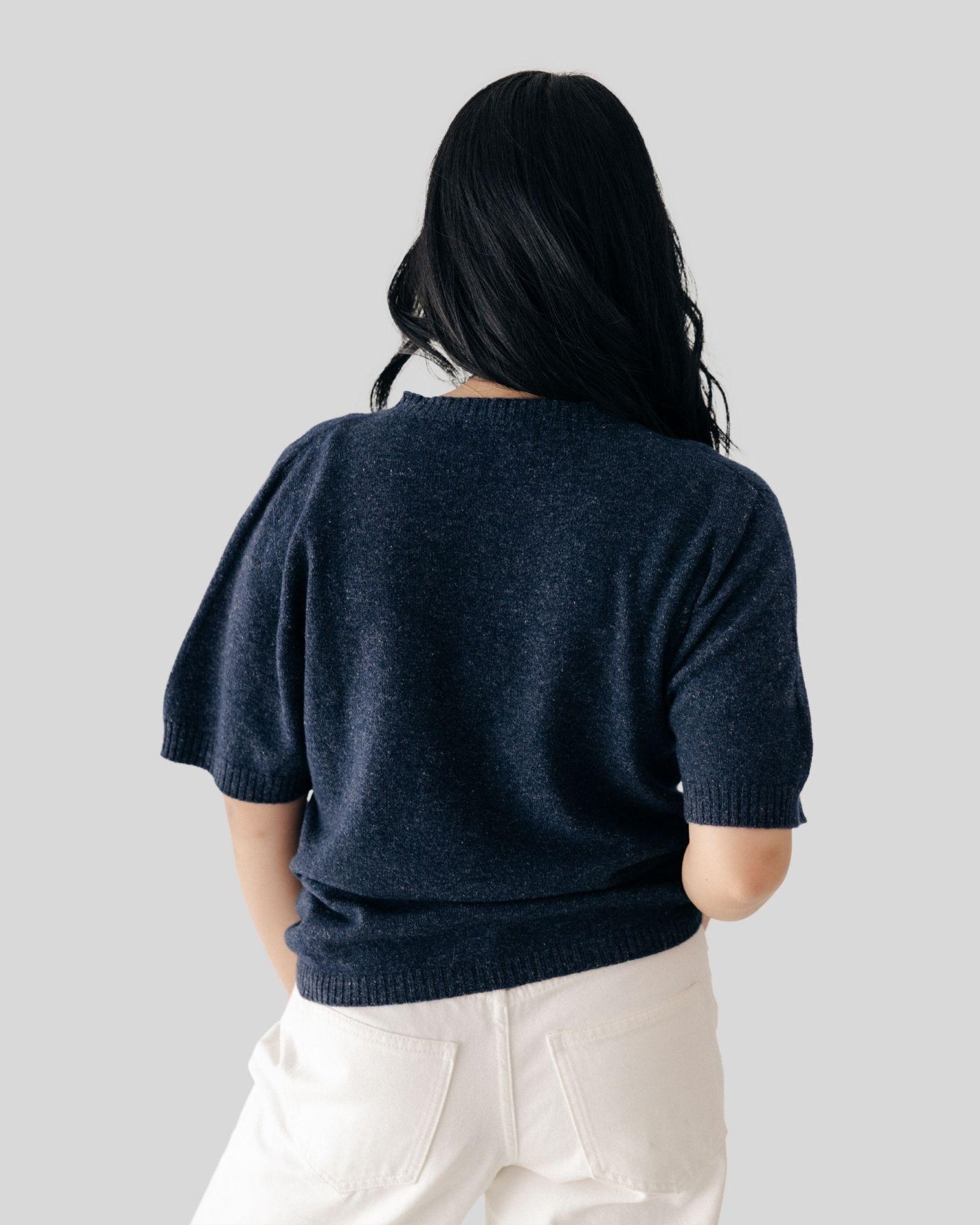 Person wearing a navy blue sweater and white pants on a light gray background