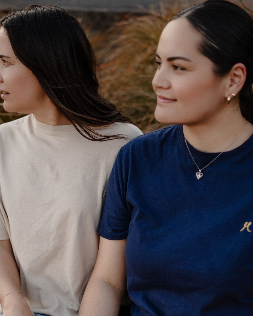 Two women sitting side by side outdoors with a natural background