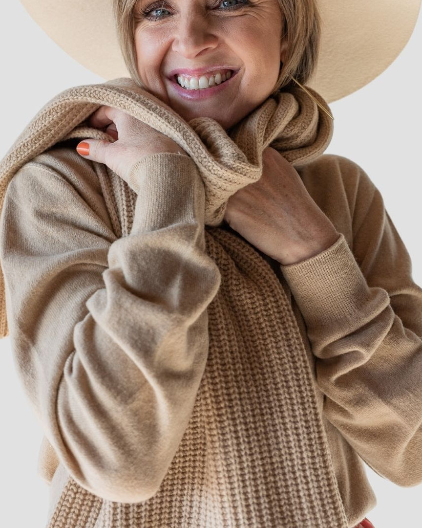 Woman wearing a beige sweater and hat with a plain background