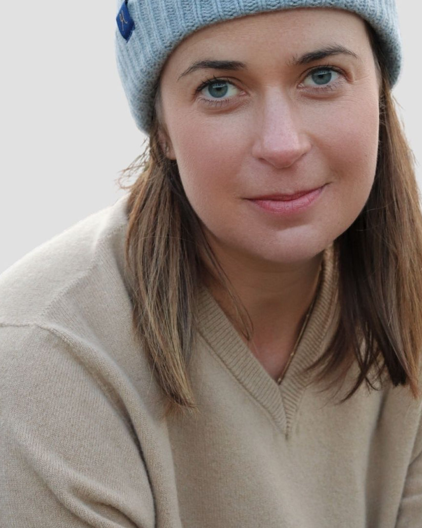 Woman wearing a light blue knit beanie and beige sweater against a plain background