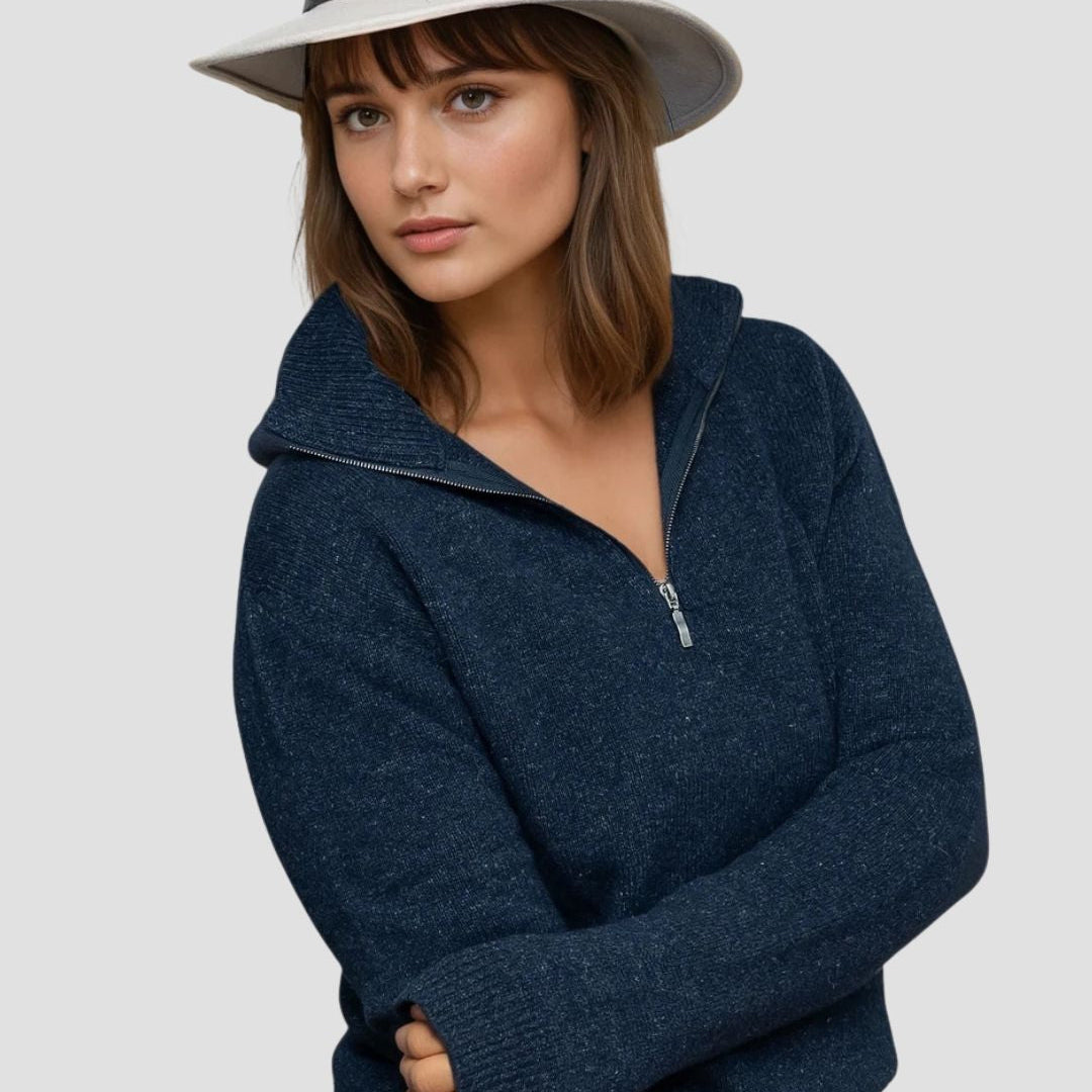 Woman wearing a navy blue zip-up sweater and white hat on a light gray background