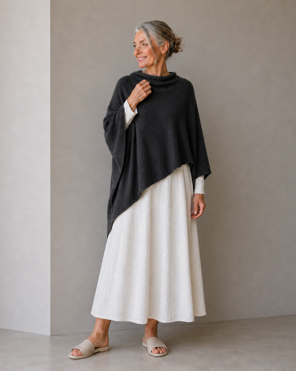 Woman wearing a black poncho over a white dress against a plain background