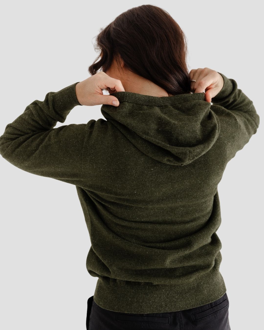 Person wearing an olive green hoodie with arms raised, on a plain background