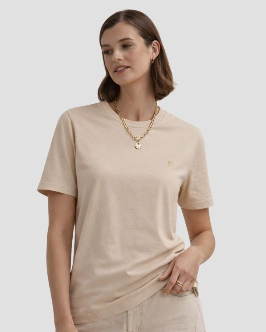 Woman wearing a beige t-shirt and gold necklace on a plain background