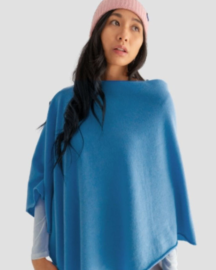 Woman wearing a blue poncho and pink beanie on a light gray background