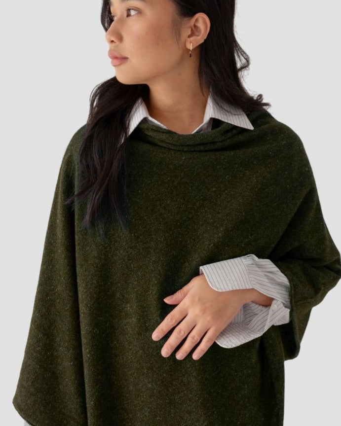 Woman wearing a green poncho over a white shirt on a light gray background