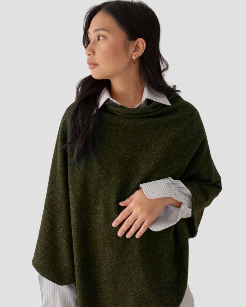 Woman wearing a green poncho over a white shirt on a light gray background
