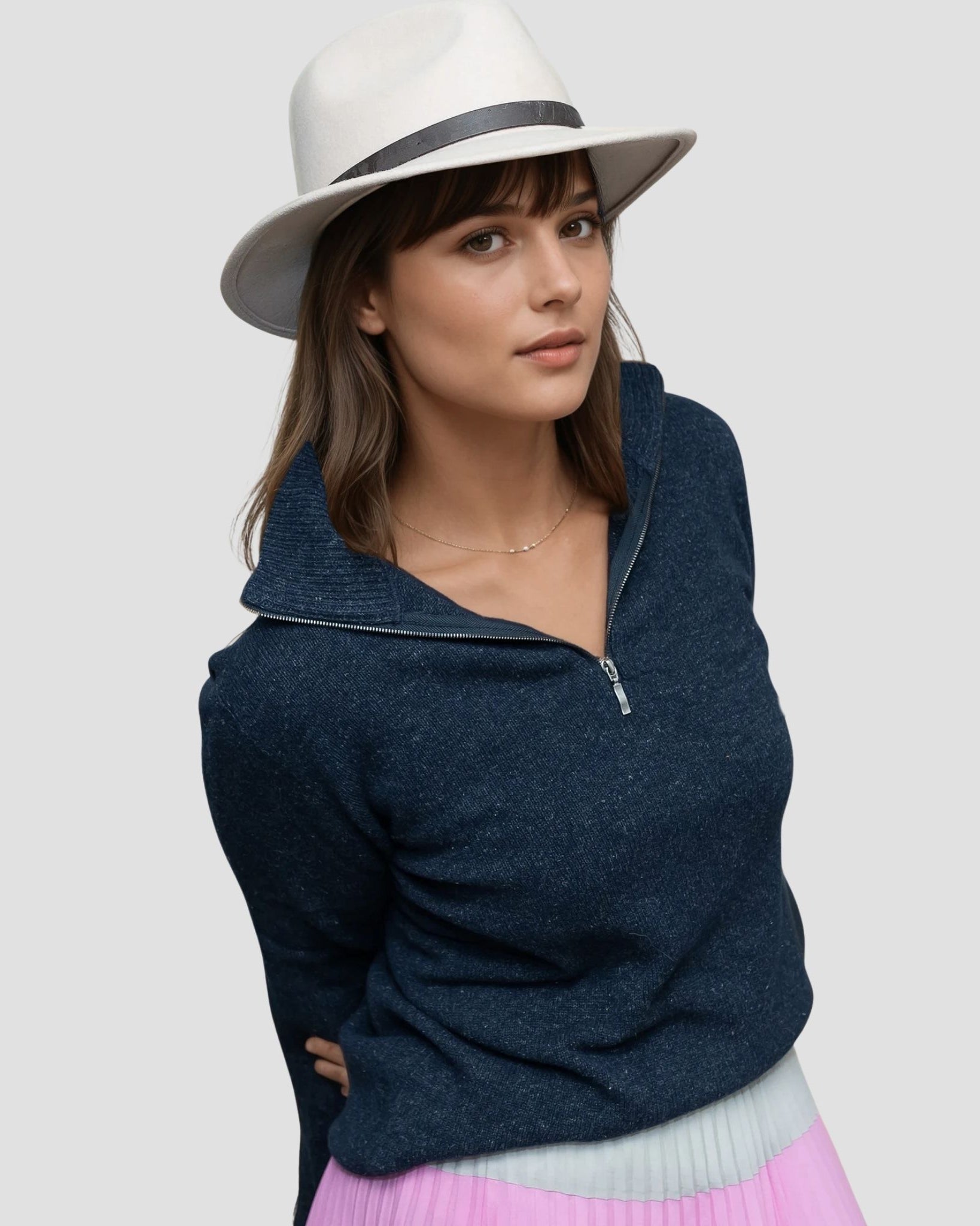 Woman wearing a navy sweater and white hat on a light gray background