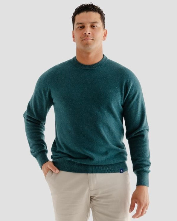 Man wearing a teal sweater and beige pants on a light gray background