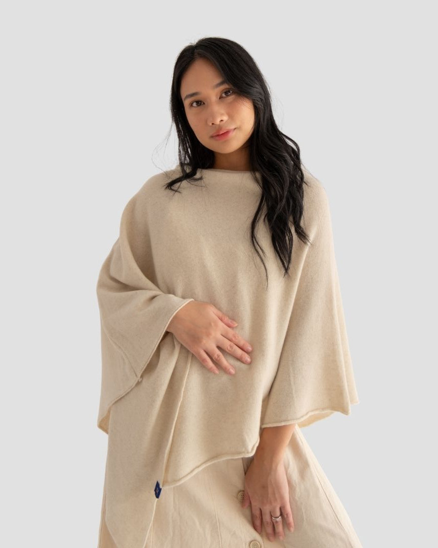 Woman wearing a beige poncho against a plain background