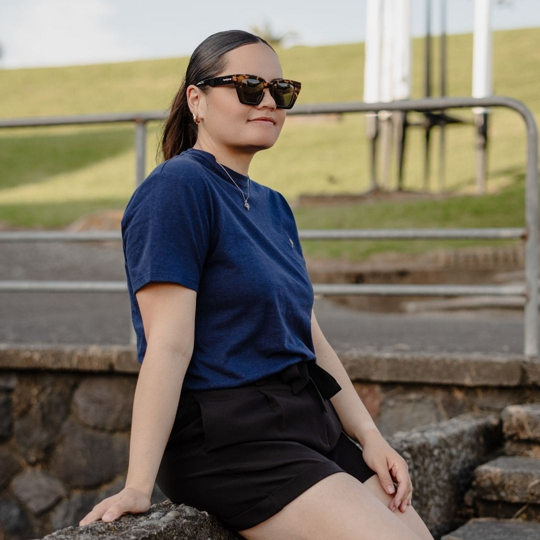 Person wearing sunglasses and a blue shirt sitting on stone steps outdoors.