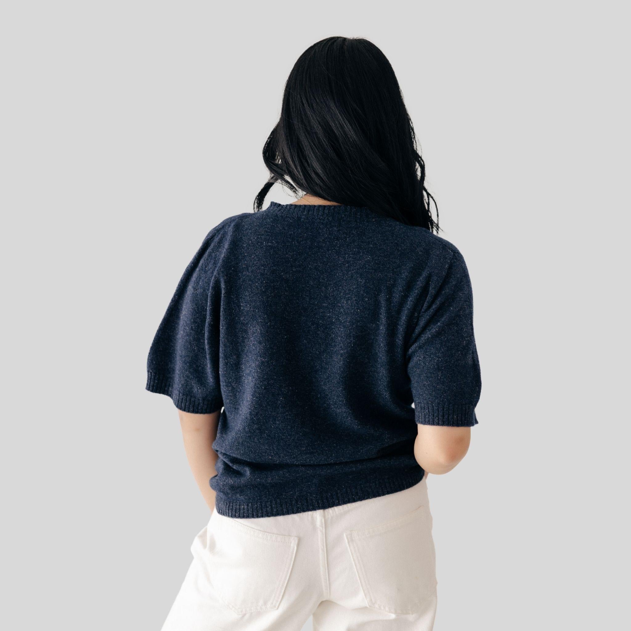 Person wearing a navy blue sweater and white pants on a light gray background