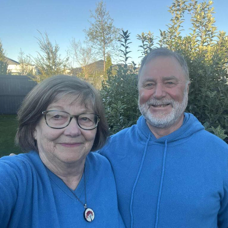 Two people wearing blue jerseys standing outdoors with greenery in the background