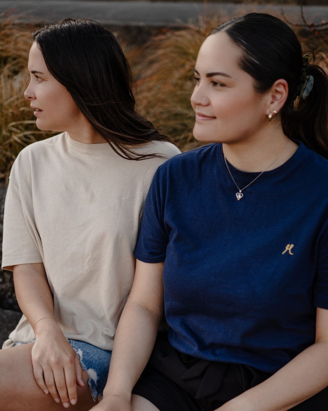 Two women sitting side by side outdoors with a natural background