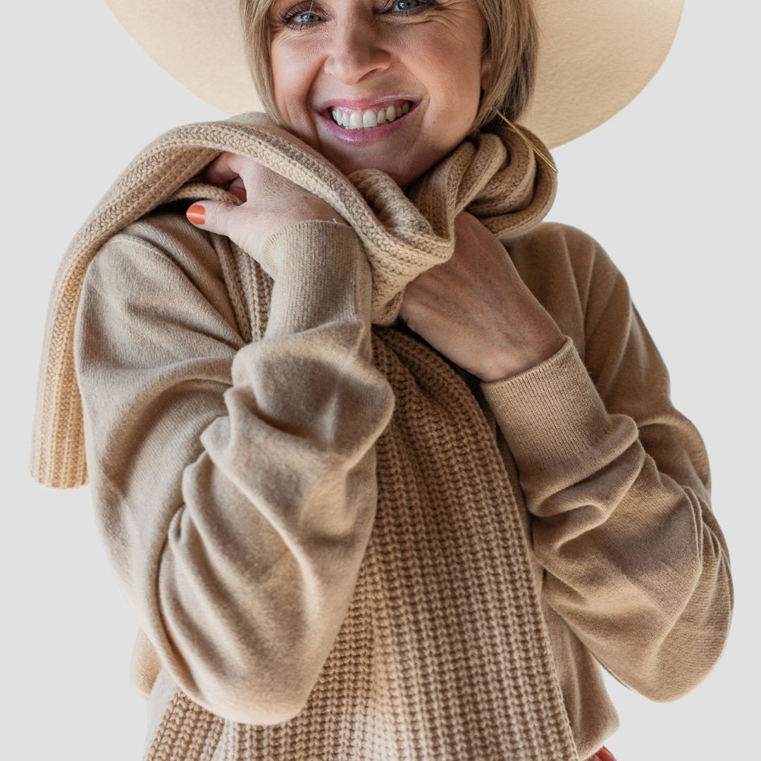 Woman wearing a beige sweater and hat with a plain background