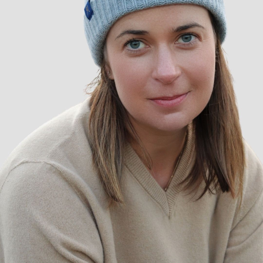 Woman wearing a light blue knit beanie and beige sweater against a plain background