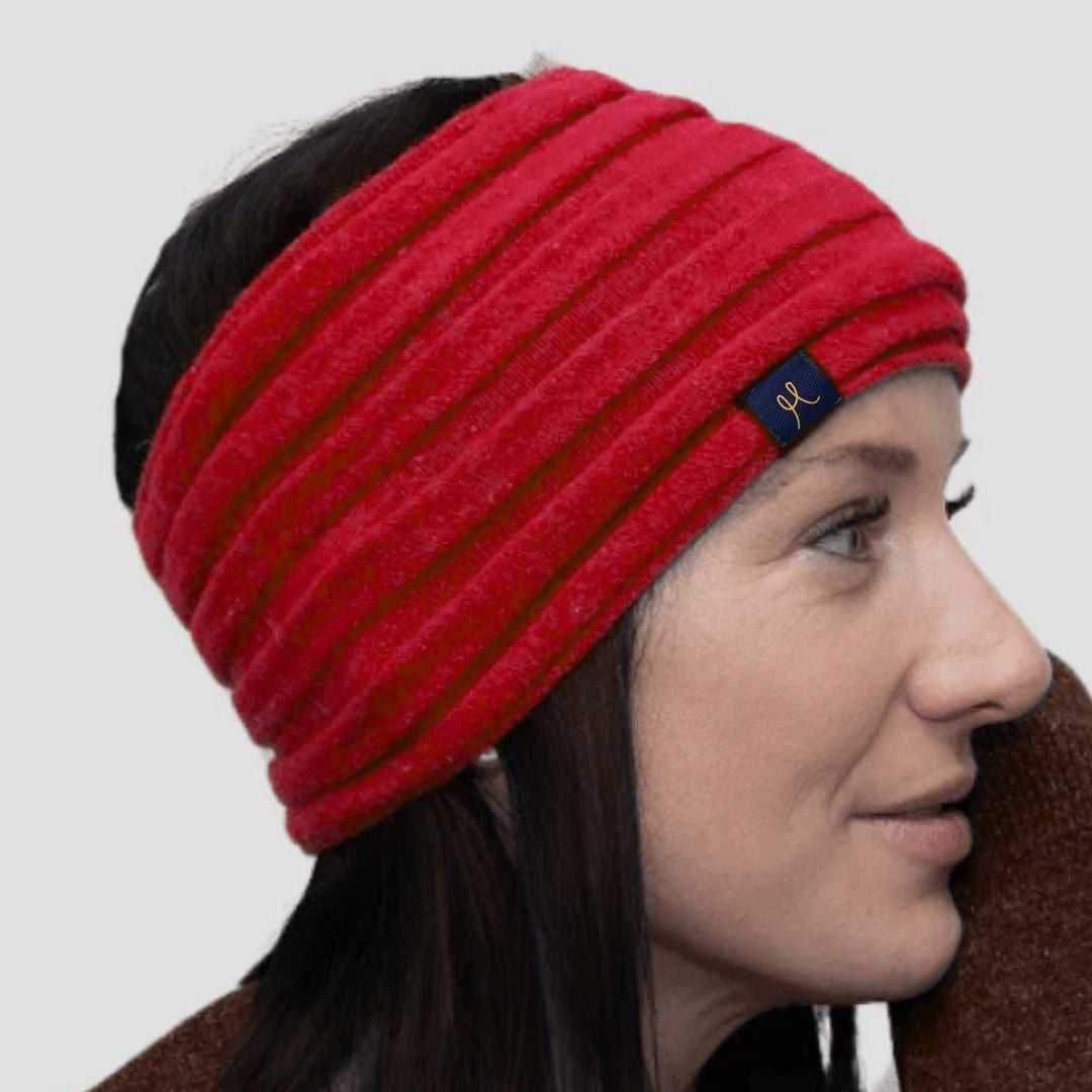 Woman wearing a red knitted headband with a brand logo on a plain background