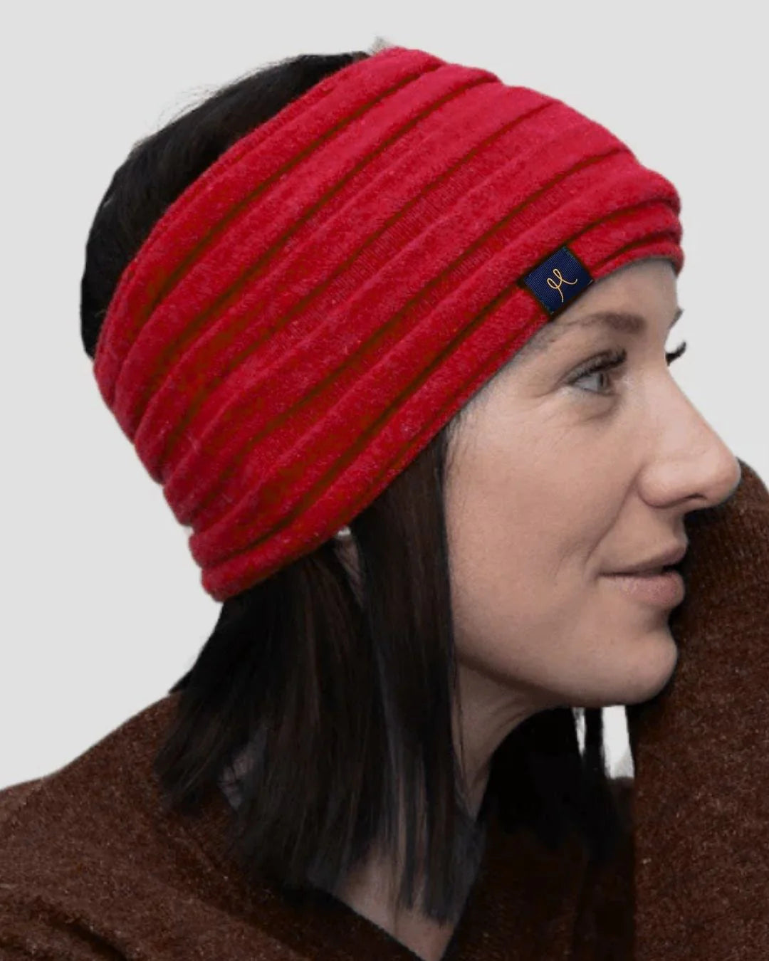 Woman wearing a red knitted headband with a brand logo on a plain background
