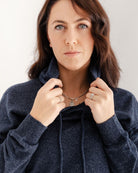 Woman adjusting the collar of a dark blue sweater against a neutral background