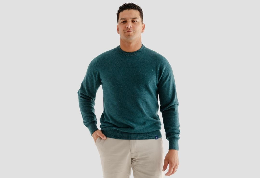 Man wearing a teal sweater and beige pants on a light gray background