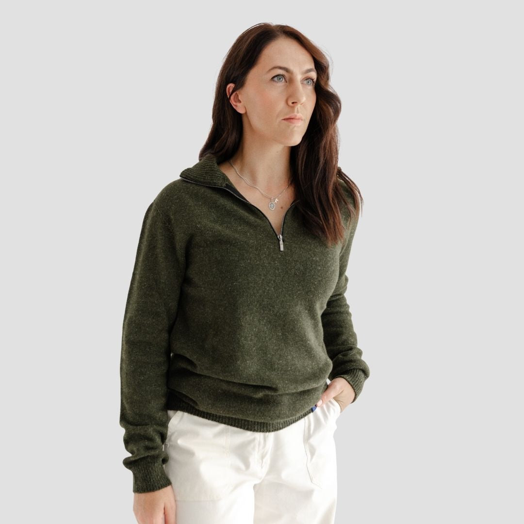 Woman wearing a green sweater and white pants against a plain background