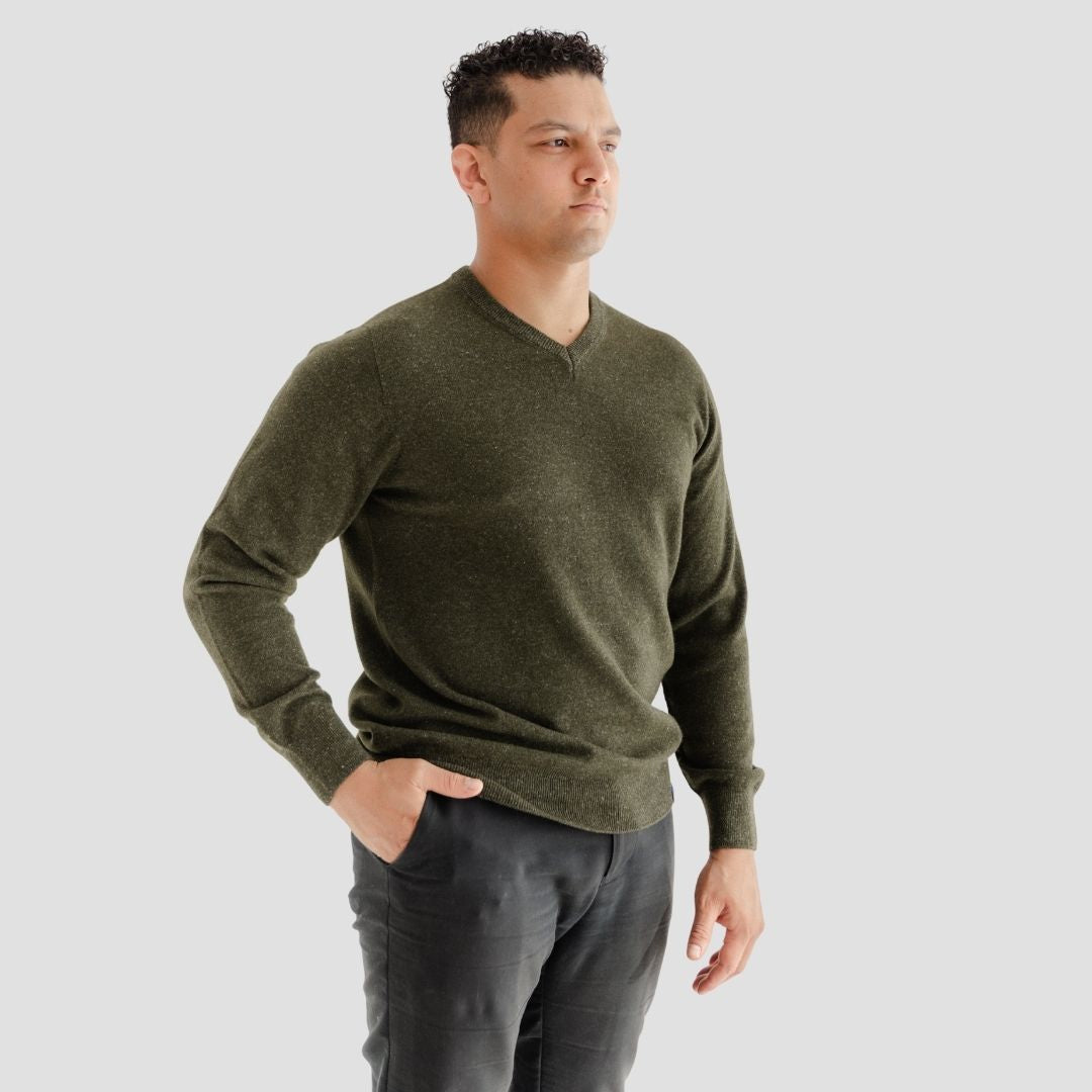 Man wearing a green sweater and dark pants against a light gray background
