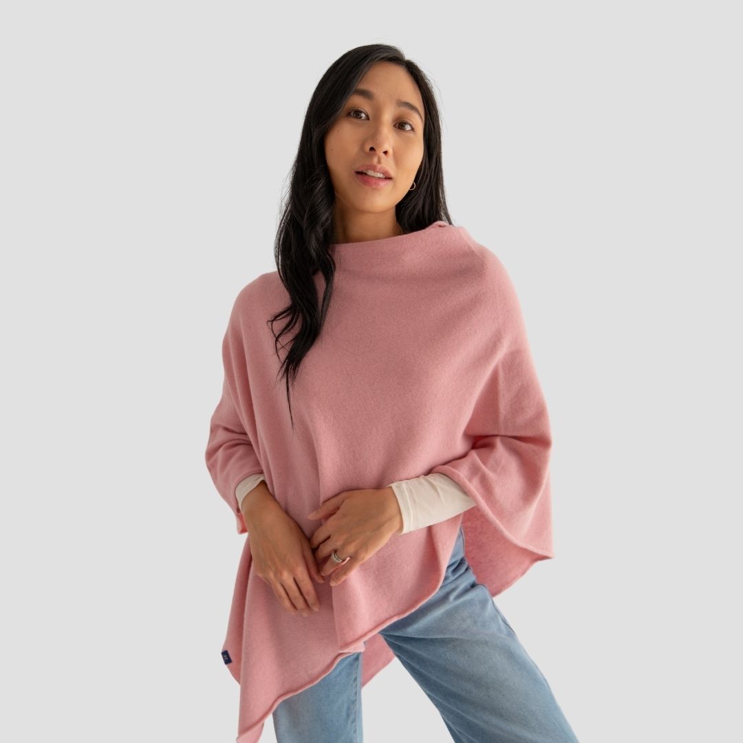Woman wearing a pink poncho over a white shirt with light blue jeans on a plain background
