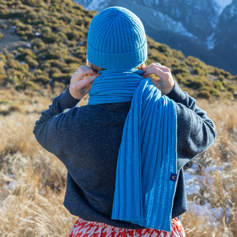 Lady looks into mountains while wearing bright blue beanie and scarf set