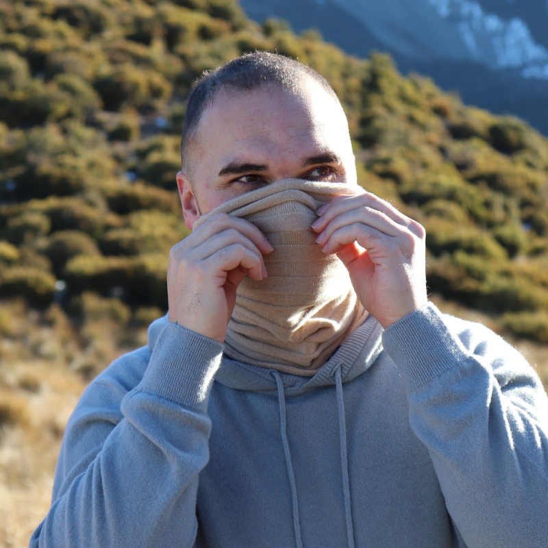 Man in mountains looking cosy comfortable in beige neck scarf keeping face warm and grey hoodie sweater. 