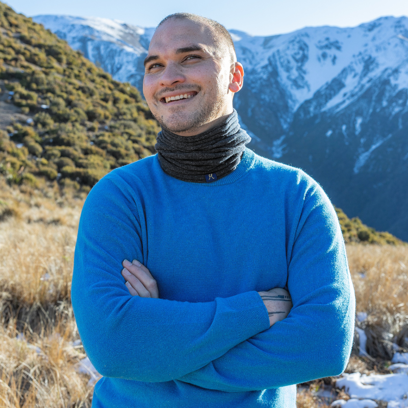 Middle aged man under New Zealand’s Southern Alps mountains wearing a bright blue sweater and charcoal grey neck buff