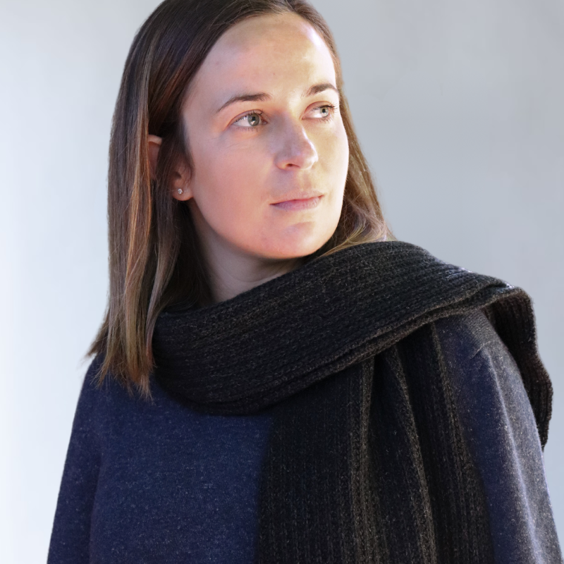 Charcoal chunky knit scarf, made from Hemp and Merino by brand Hemprino. Wearing with Navy V neck sweater jersey jumper. Thirty year old girl looking fashionable and confident.