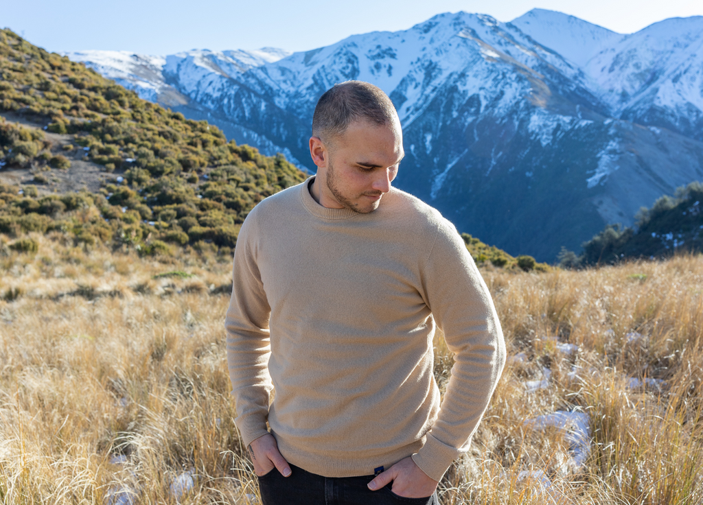 Man in beige hemp and merino blend hemprino jersey crew neck in mountain area with tussock and snow. looking warm and cost.