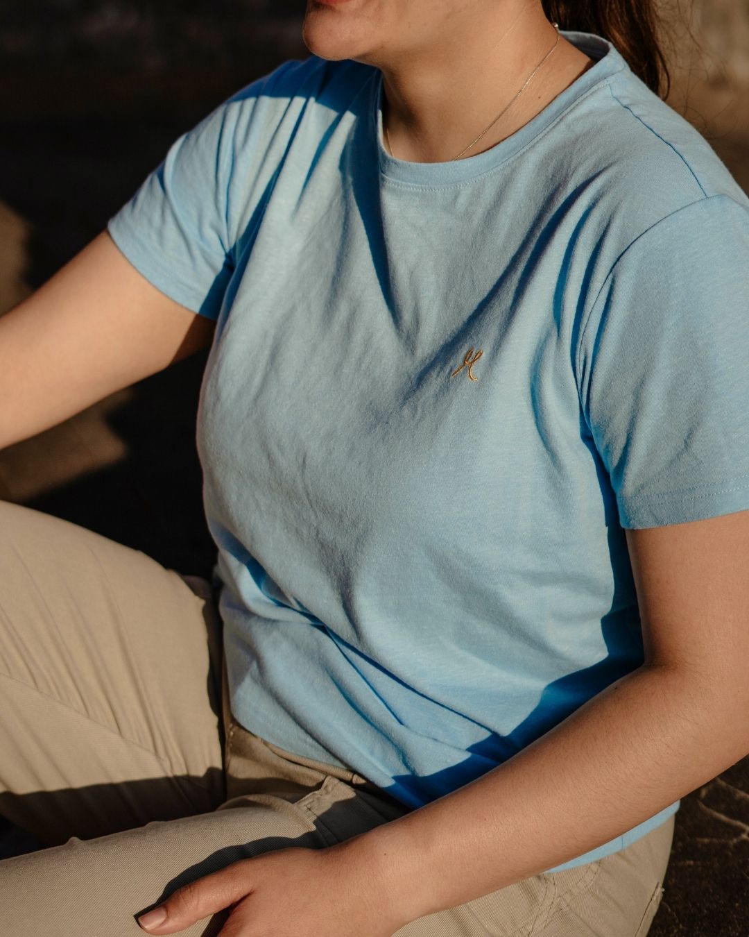 Person wearing a light blue t-shirt with a small logo, sitting on a couch.