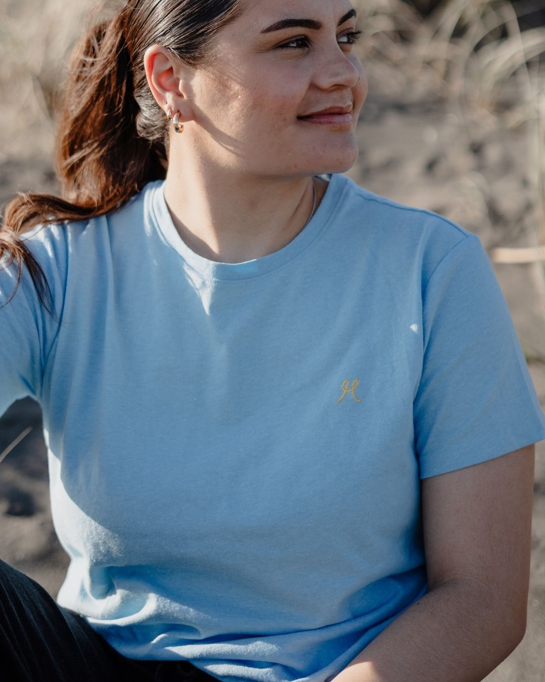 Woman wearing a blue t-shirt with a logo, sitting outdoors.