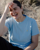 Woman in a blue t-shirt sitting outdoors with a blurred natural background