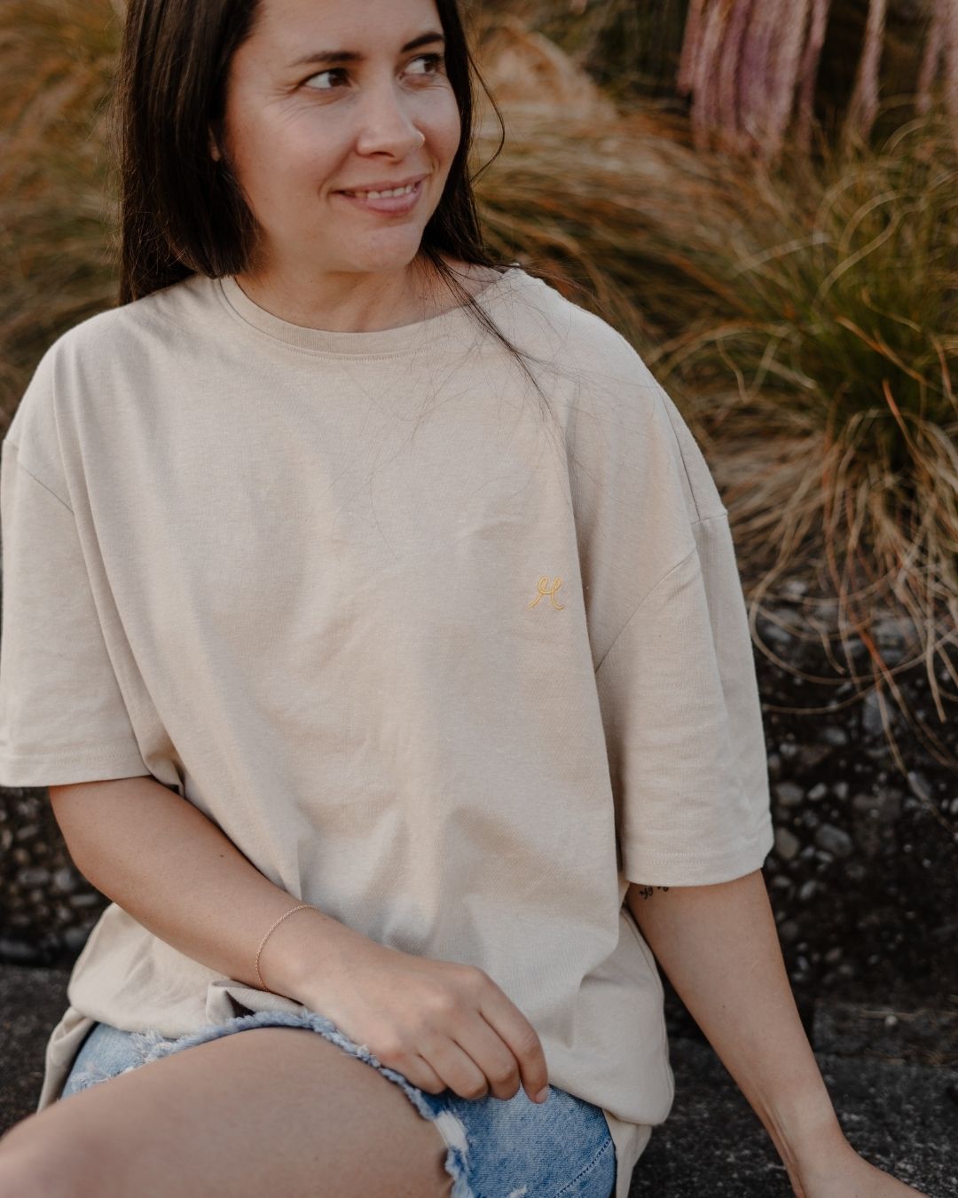 Woman wearing a beige t-shirt sitting outdoors with grass in the background