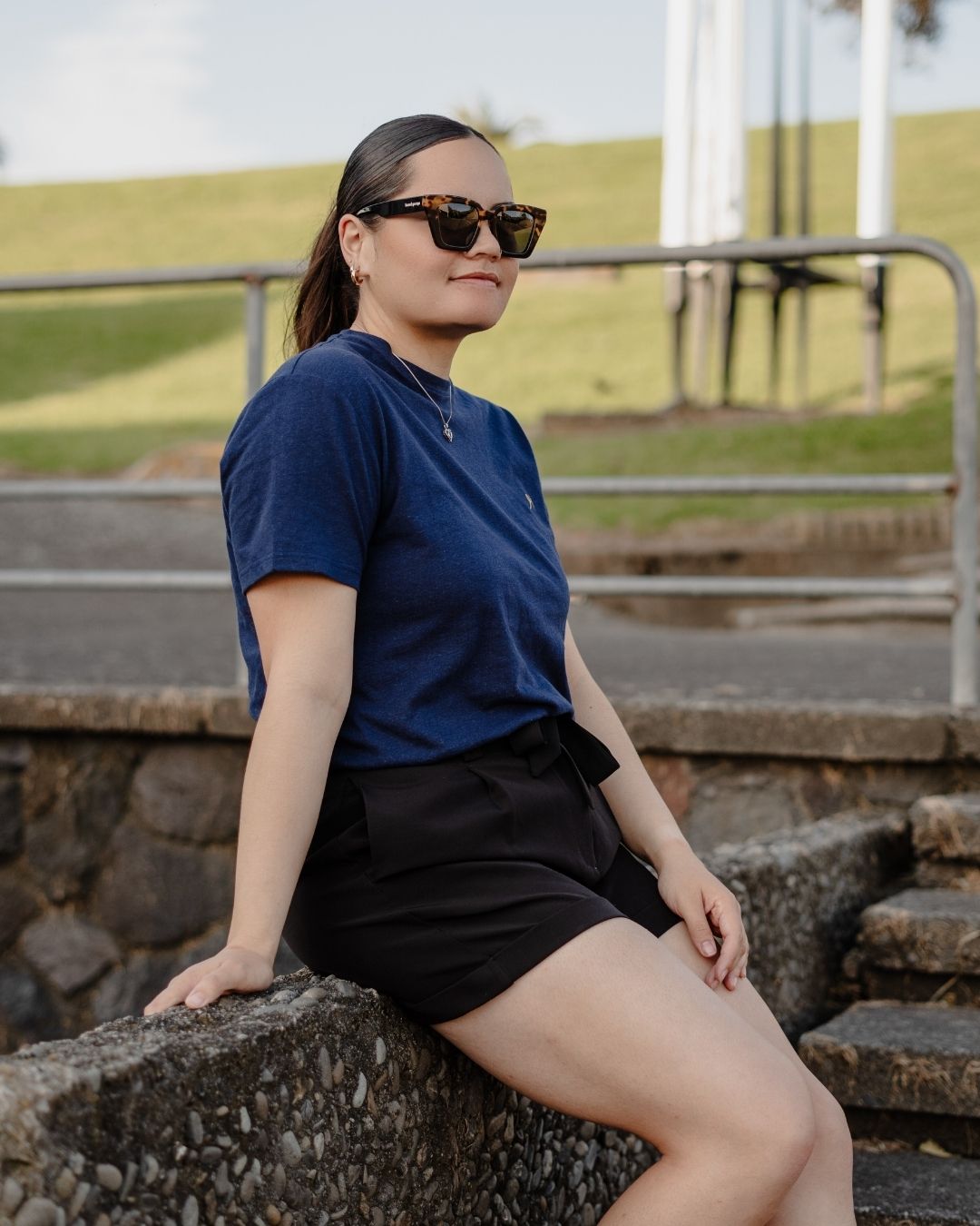 Person wearing sunglasses and a blue shirt sitting on stone steps outdoors.