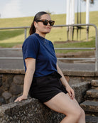 Person wearing sunglasses and a blue shirt sitting on stone steps outdoors.