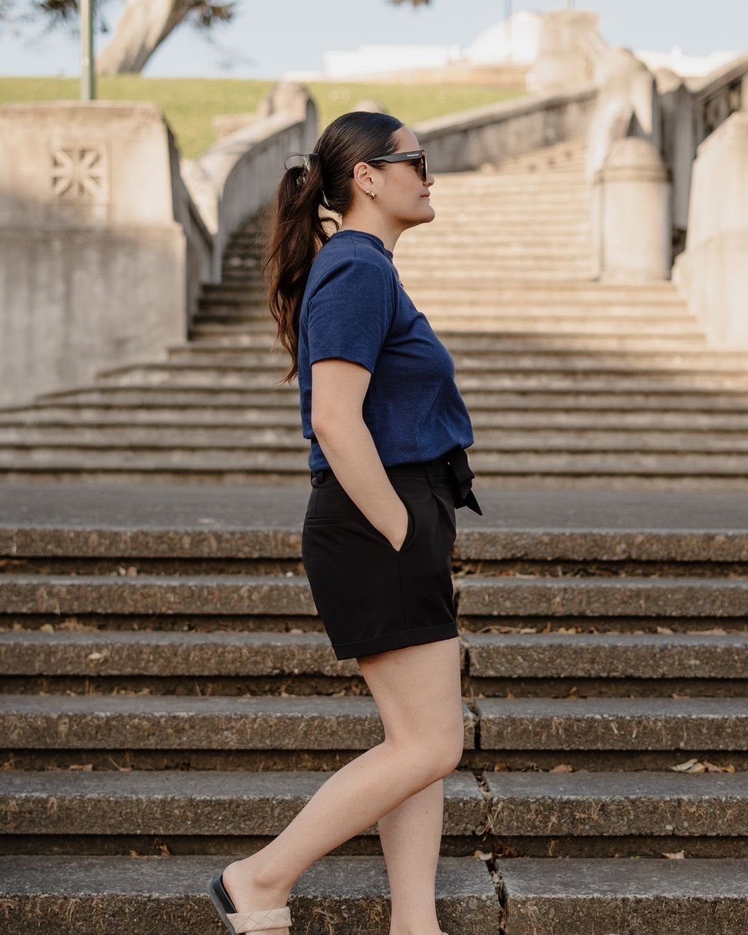 Woman in a blue shirt and black shorts standing on stone steps with a scenic background
