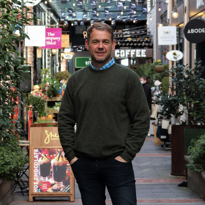 Middle aged man looking well dressed in a green crew neck jersey from brand Hemprino. Made from hemp and merino. Paired with tidy jeans and hands in pocket. Looking smart but casual. Out to enjoy drinks with friends.