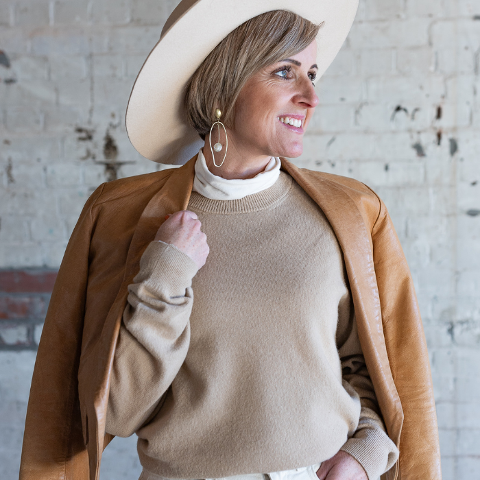 Blonde lady wearing beige crew neck jersey and leather jacket looking stylish and relaxed. 