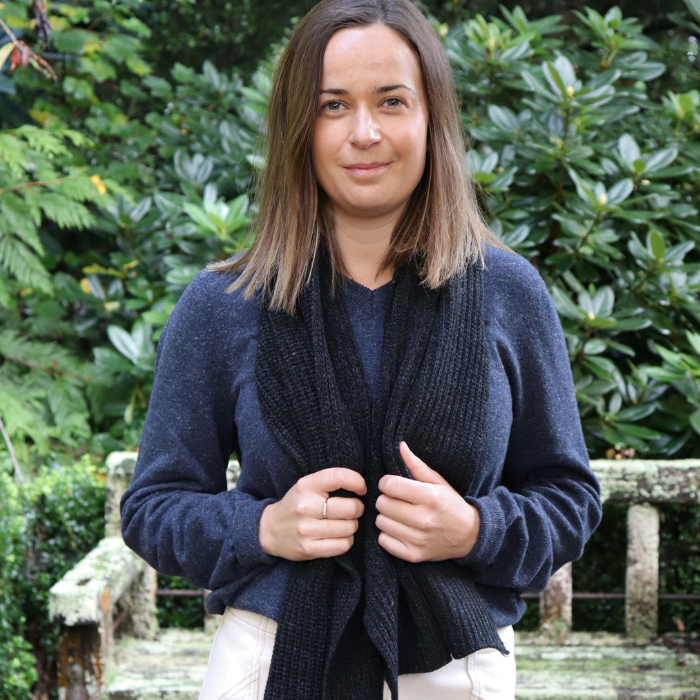 Charcoal chunky knit scarf, made from Hemp and Merino by brand Hemprino. Wearing with Navy V neck sweater jersey jumper. Thirty year old girl looking fashionable and confident.