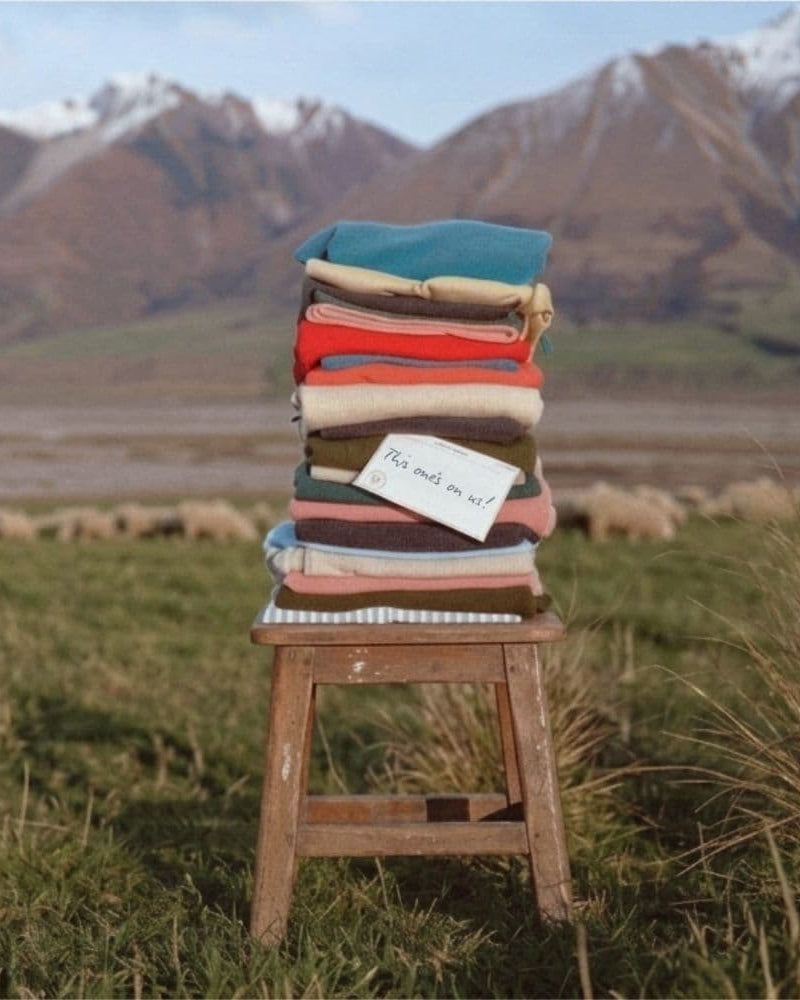 Chair with a colorful sweaters in a field with mountains in the background